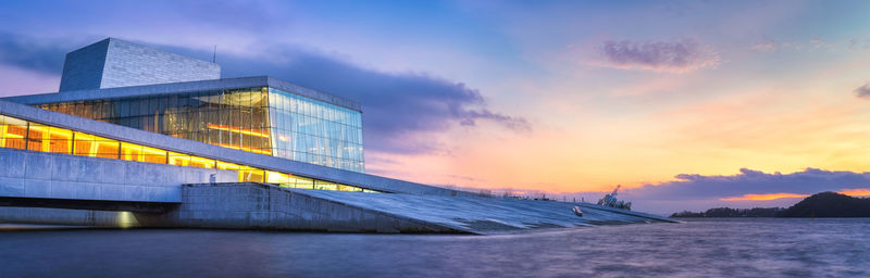 Building by river against sky at sunset