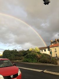 Rainbow over road by building against sky