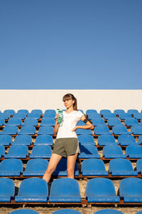 Full length of woman sitting on seat against clear blue sky