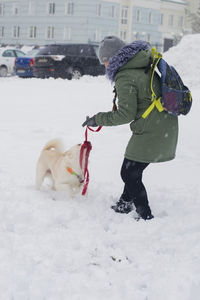 Side view of woman playing with dog in snow