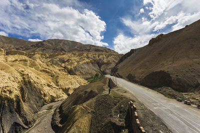 Rear view of man on road amidst mountains against sky