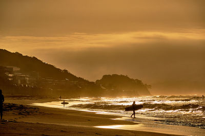 Silhouette man with surfboard on beach against sky during sunrise