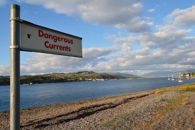 Information sign by sea against sky