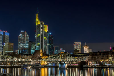 Illuminated buildings by river against sky in city at night