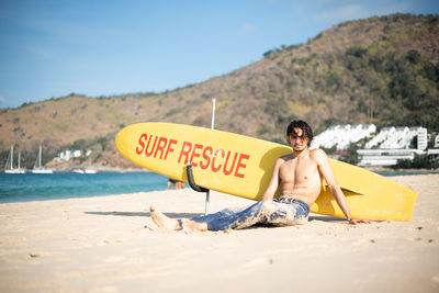 Full length of shirtless man sitting on beach