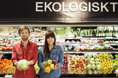 Portrait of young couple holding fresh vegetables in supermarket