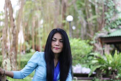 Thoughtful beautiful woman standing against trees in forest