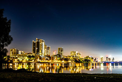 Illuminated buildings by river against sky at night