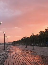 Footpath by street against sky during sunset