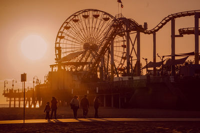 People at amusement park against sky during sunset