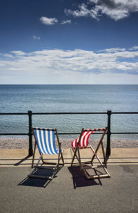 Blue and red empty deck chairs against sea on sunny day