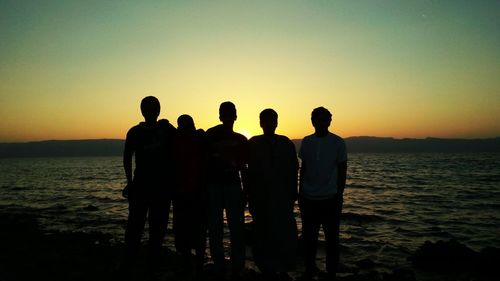 Silhouette men standing by sea against sky during sunset