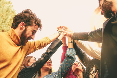 Low angle view of friends raising hands against clear sky