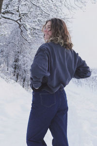Young beautiful woman standing on snow covered land, looking over shoulder laughing
