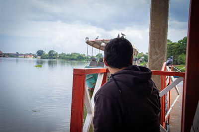 Rear view of man standing by railing against sky