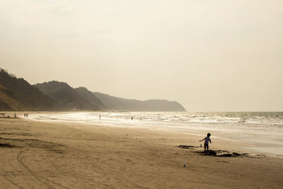 Boy standing at beach against sky