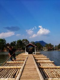 People on pier over lake against sky