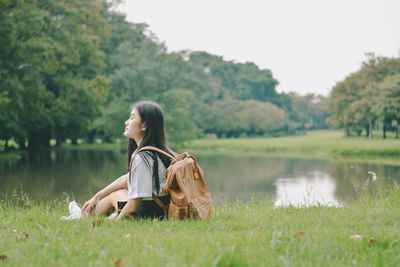 Woman sitting on grassy field against lake