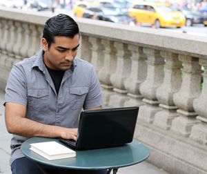 Young man using laptop at sidewalk cafe