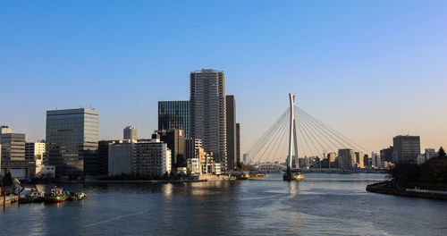 Panorama of sunset sumida river in tokyo with hanging bridge, boats and skyscrapers
