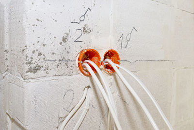 Orange, round junction box mounted in the white wall with protruding electric cables.