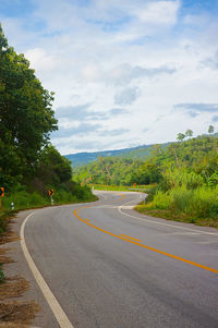 Empty road along trees and plants against sky