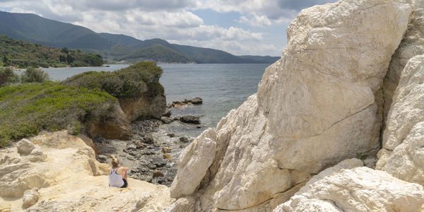 Rear view of woman sitting on rock at beach