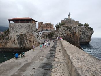 People walking on building by sea against sky