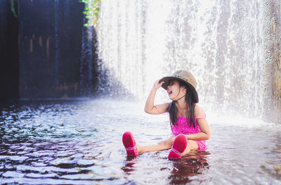 Cute girl sitting against waterfall