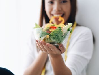 Portrait of young woman holding salad in bowl while sitting at home
