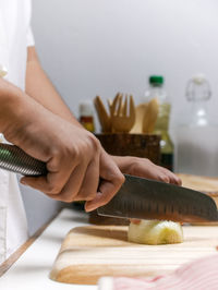 Midsection of chef chopping onion slice on cutting board with kitchen knife