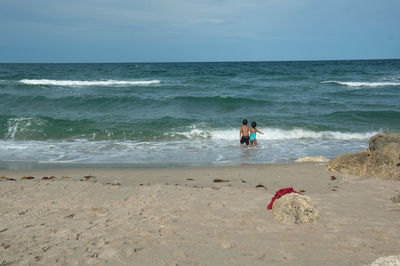 Rear view of siblings standing on shore at beach