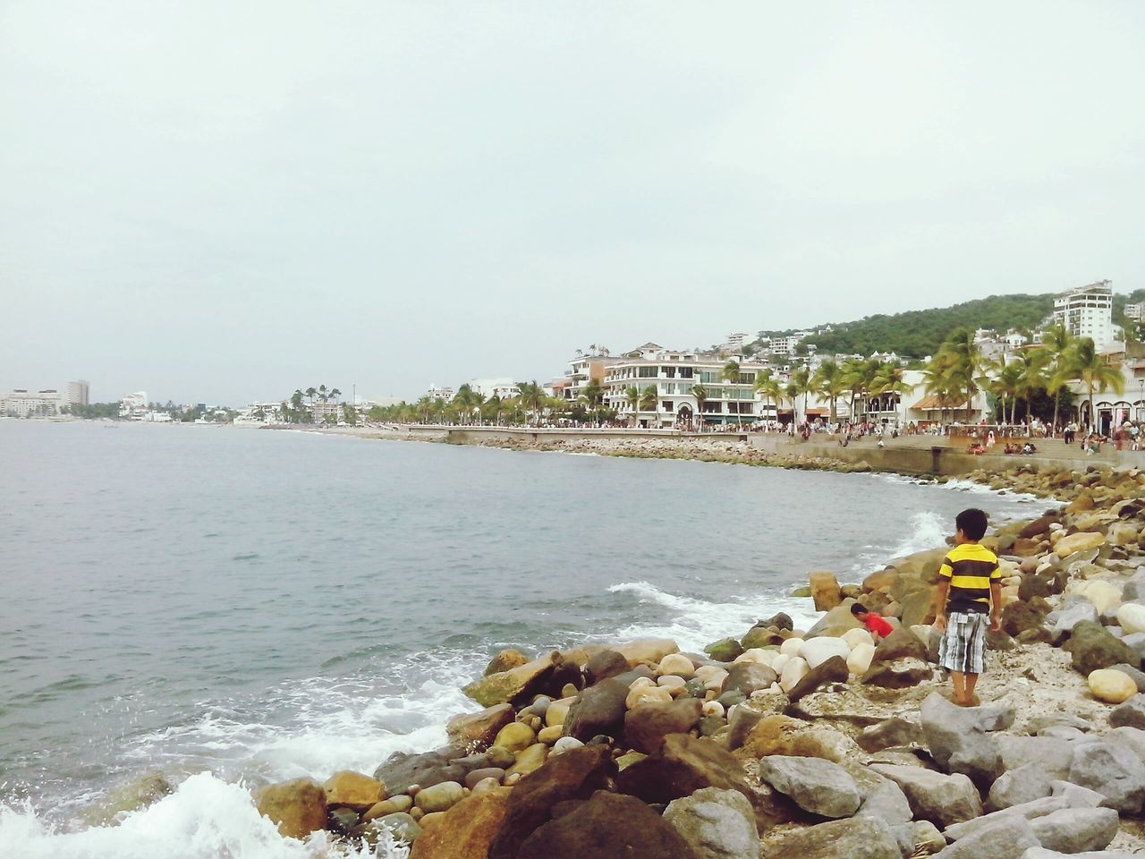 water, lifestyles, leisure activity, sea, men, rock - object, building exterior, built structure, architecture, clear sky, person, beach, shore, walking, copy space, sky, large group of people, nature, day