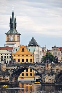 Arch bridge over river by buildings against sky in city