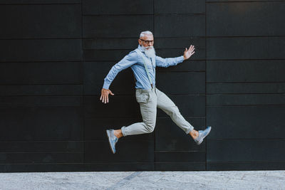 Senior hipster jumping against wall