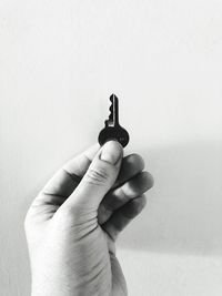 Close-up of human hand holding key against wall