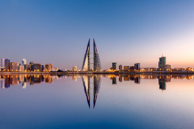 Reflection of illuminated buildings in water against bahrain skyline