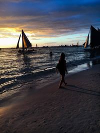 Woman walking at beach against sky during sunset