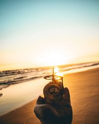 Close-up of hand on beach against sky during sunset