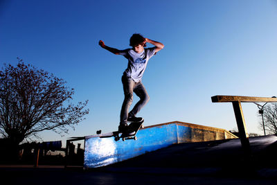 Full length of boy skateboarding against clear blue sky during sunset