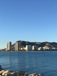 Sea by buildings against clear blue sky