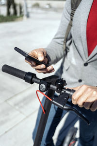 Midsection of businessman using mobile phone while standing with push scooter