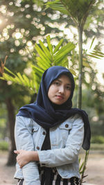 Portrait of young woman standing against trees