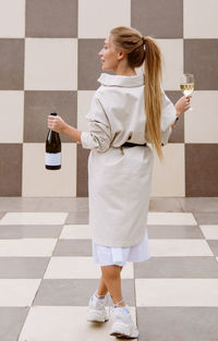 Young woman tasting white wine against chessboard background