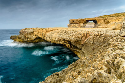 Rock formation by sea against sky