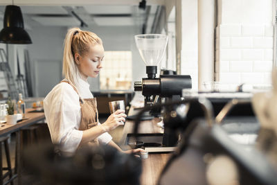 Female barista holding container by coffee maker at counter in cafe