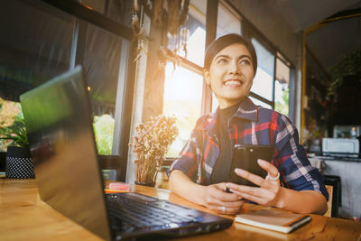 Young woman using phone while sitting on table