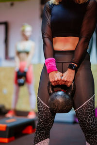Midsection of woman holding kettlebell while standing in gym