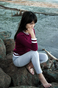 Full length of girl sitting on rock by river