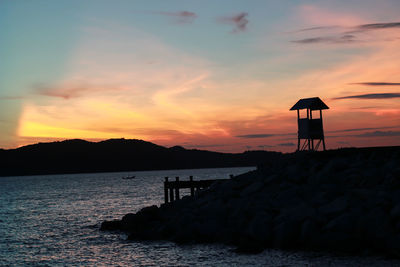 Silhouette rocks by sea against sky during sunset